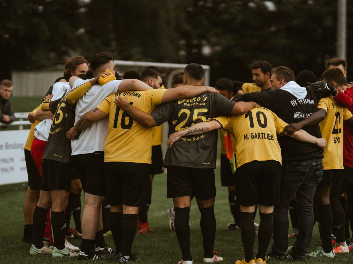 Eine Fußballmannschaft in gelb-schwarzen Trikots steht im Kreis auf dem Platz